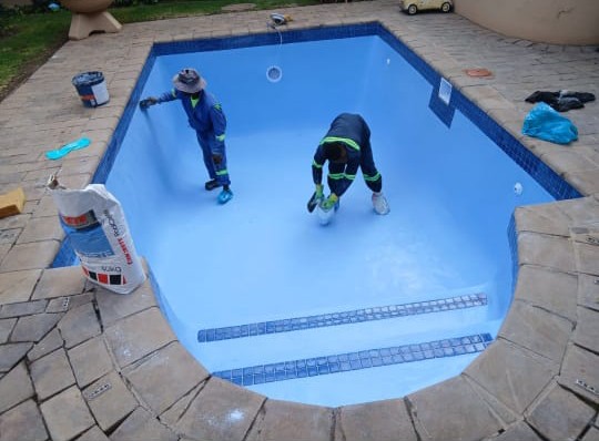 Team applying a fresh interior finish inside an empty swimming pool during renovation