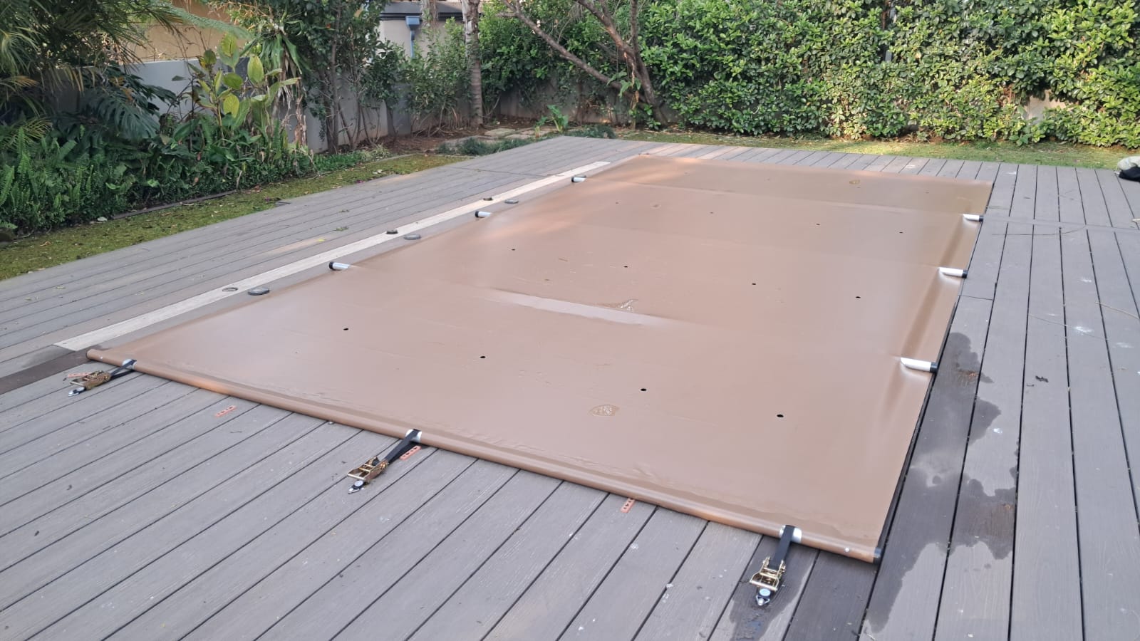 Pool safety cover fitted and tensioned over a pool on a timber deck